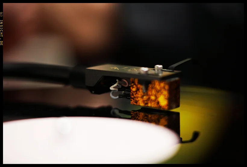 Close-up of a phono cartridge riding a spinning record in warm amber light.