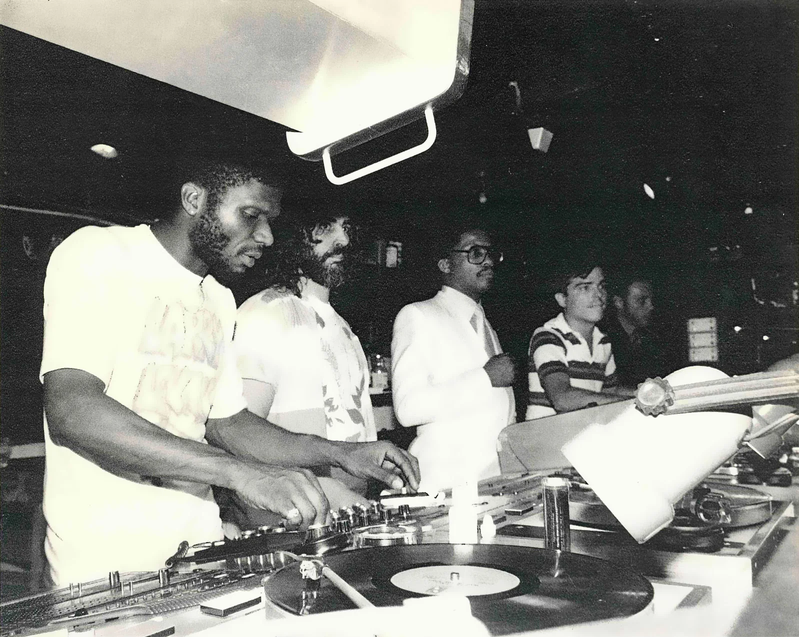 Black-and-white photograph at the Paradise Garage: Larry Levan at the turntables, David Mancuso beside him, Herbie Hancock looking on.